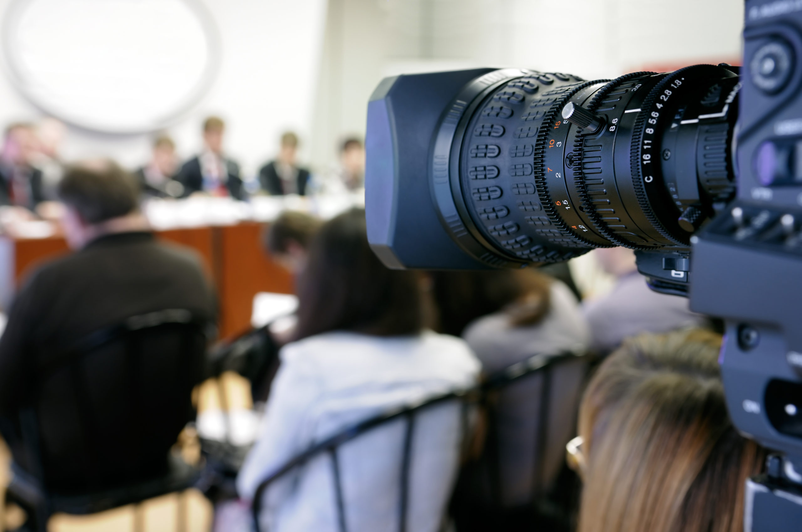 Lens of TV camera against the background of press conference.