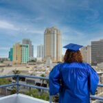 College graduate in cap and gown looking at city skyline from roof