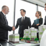 Business people shaking hands over model of proposed real estate project