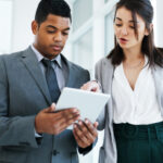 Young male and female business professionals standing next to each other and looking at something on a tablet